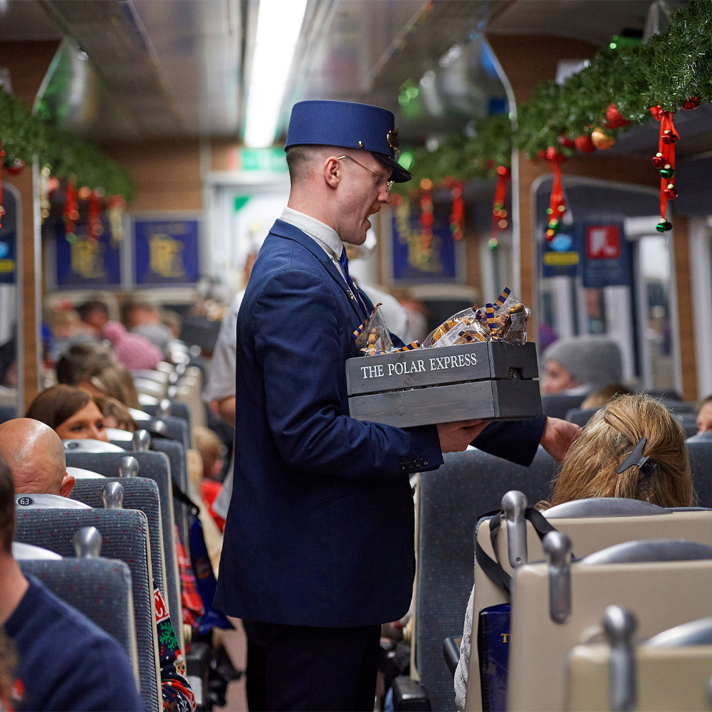 The Polar Express Train Ride Conductor on board the train with a grey wooden box handing out cookies