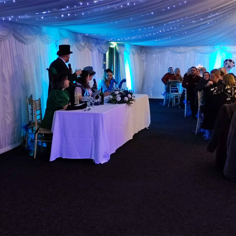 Photo of diners watching the murder mystery event long table at side of the room round tables with candles in white tent with fairy lights